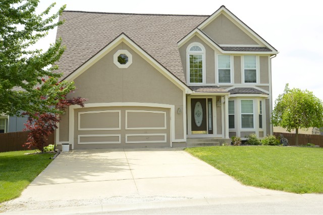 A gray modern home with white trim in Aurora, IL with green grass and a white concrete driveway.