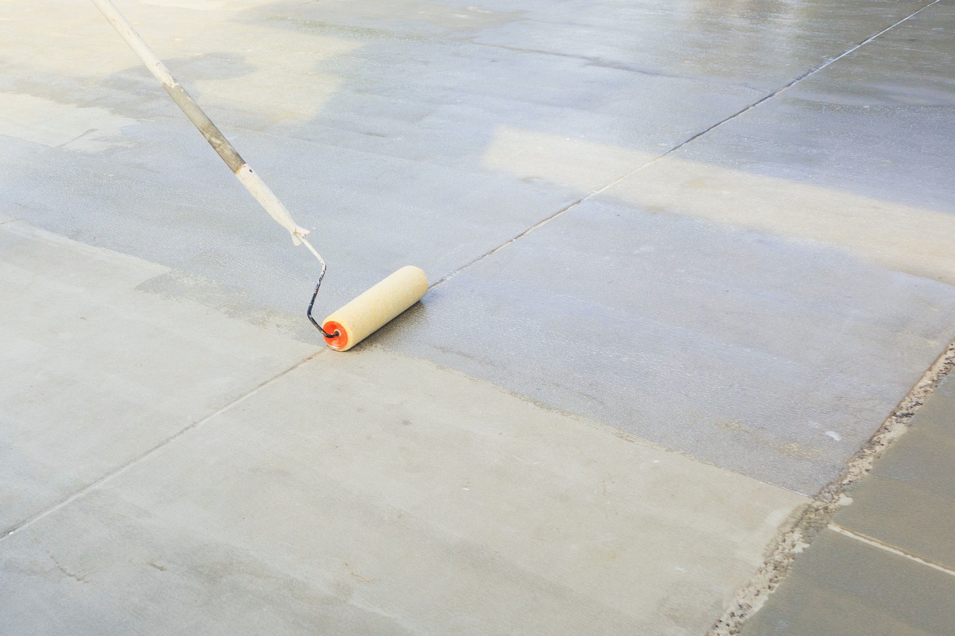 A person in Aurora, IL using a roller to apply concrete sealer to a driveway.