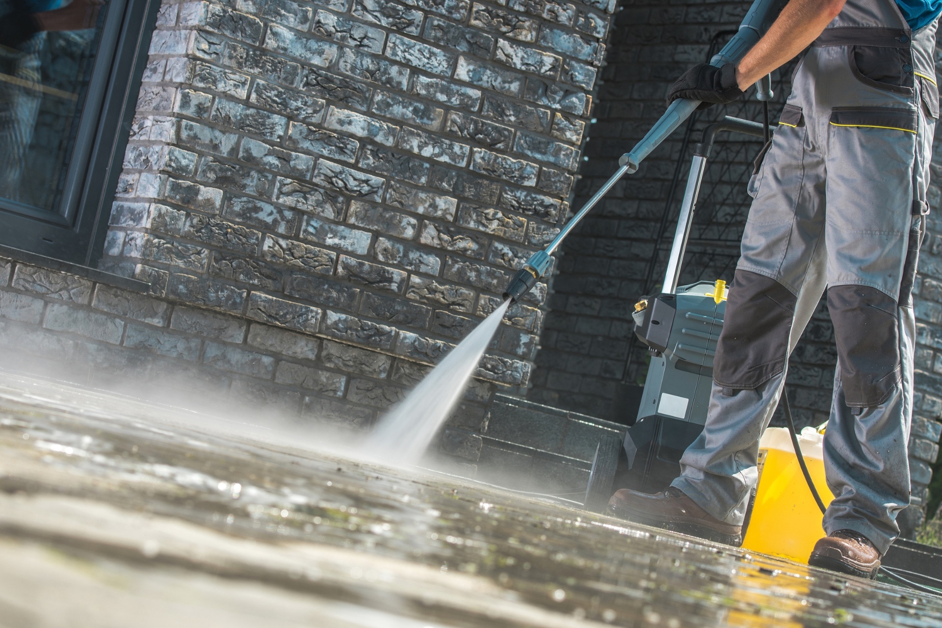 A man standing in front of his home pressure washing his concrete driveway.
